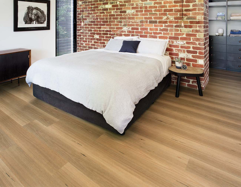 Bedroom with a bed against a brick wall, wooden floor, and side table.