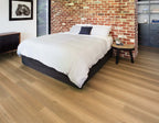 Bedroom with a bed against a brick wall, wooden floor, and side table.