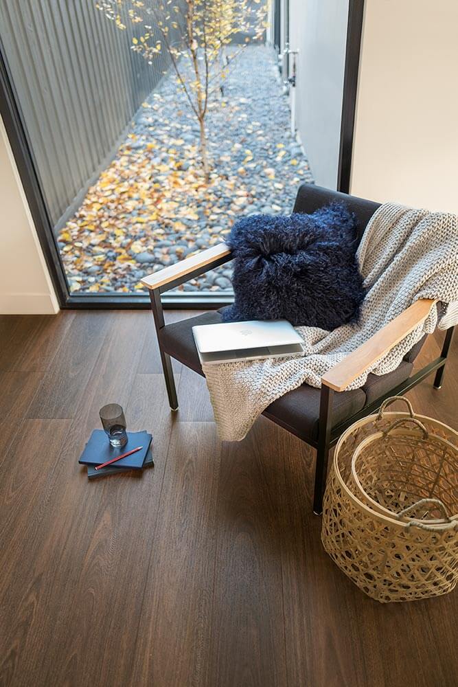 Chair with a blanket and pillow by a sliding glass door with a view of a garden.