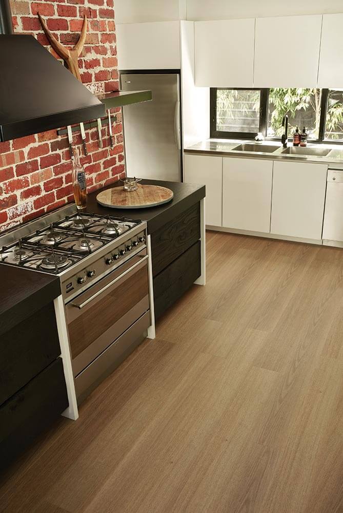 Modern kitchen with wooden flooring, brick wall, and stainless steel appliances.
