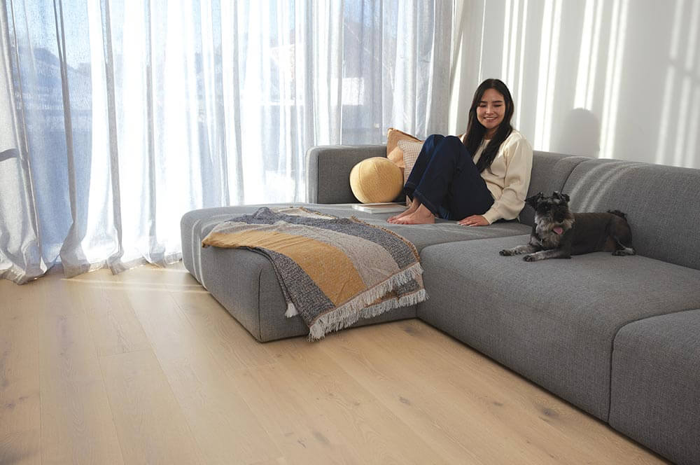 Woman sitting on a gray sectional sofa with a dog in a bright living room.