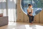 Person sitting on a concrete ledge with a large circular window in a modern interior.