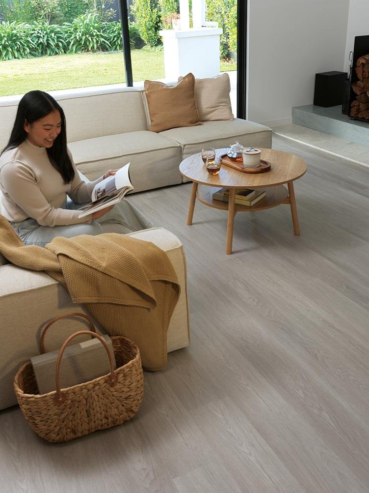 Woman reading a book on a beige sofa in a modern living room with a wooden coffee table.