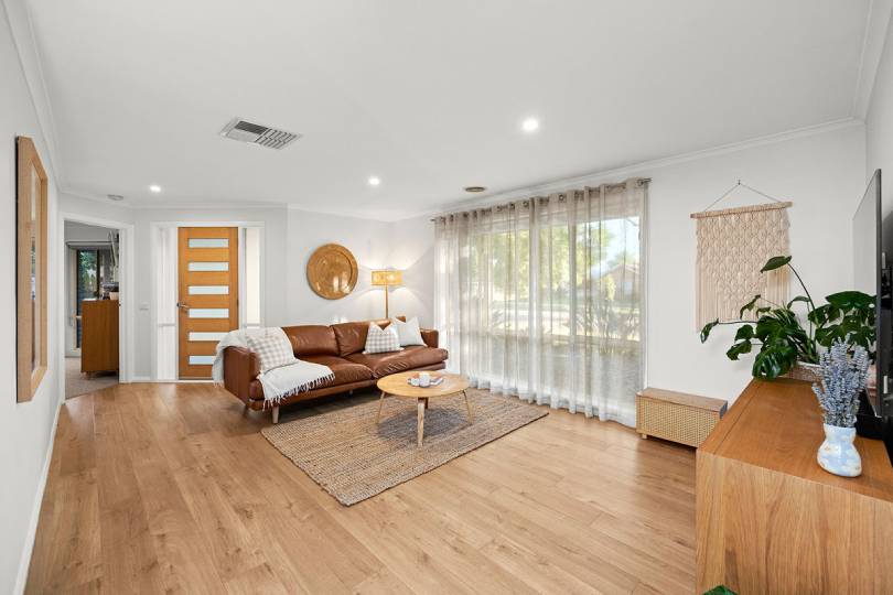 A bright and inviting living room with light blonde timber flooring that creates a warm, airy feel, styled with a tan leather sofa, natural jute rug, oak furniture, and sheer curtains that flood the space with beautiful natural light.