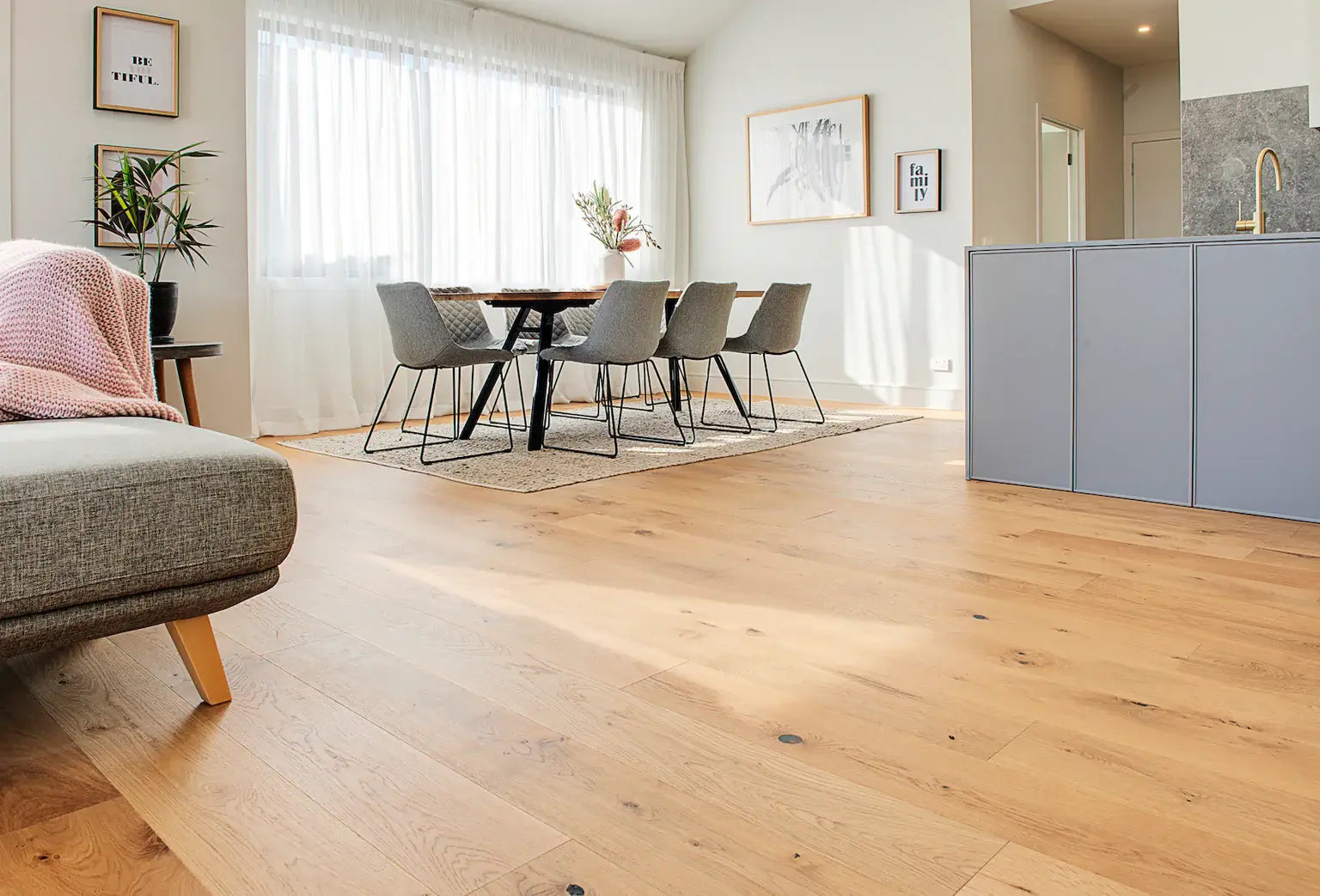 Modern living room with wooden floor, gray sofa, and kitchen area.
